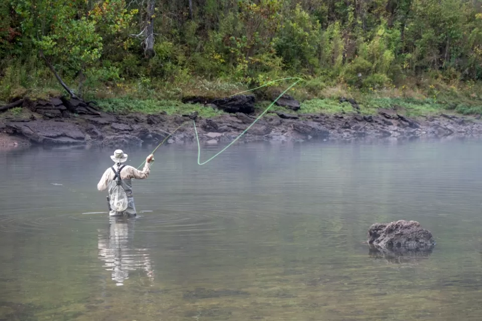 A fly fisher casts on a fog-covered river.